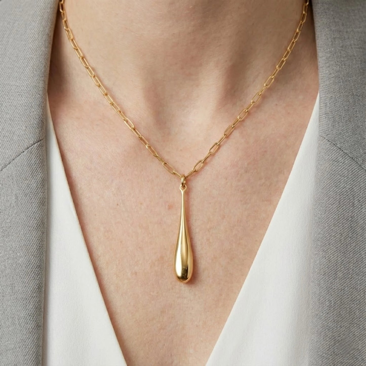 Modern gold teardrop pendant necklace in 18K gold plated stainless steel, worn on model with grey blazer