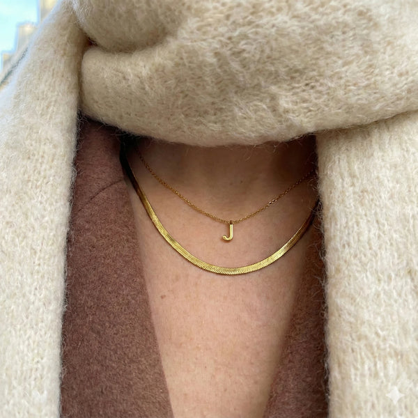 Woman in a cream scarf and brown coat wearing the Kaia herringbone necklace in 18K gold-plated waterproof stainless steel