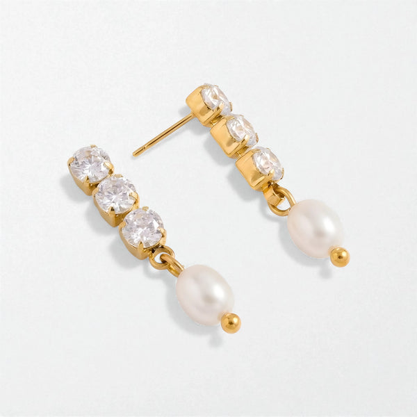 Gold earrings with clear gemstones and pearls on a light gray background