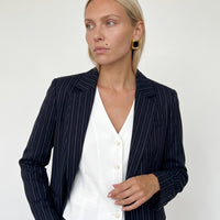 Woman in a navy pinstripe blazer and white vest wearing Sabine black and gold square statement stud earrings