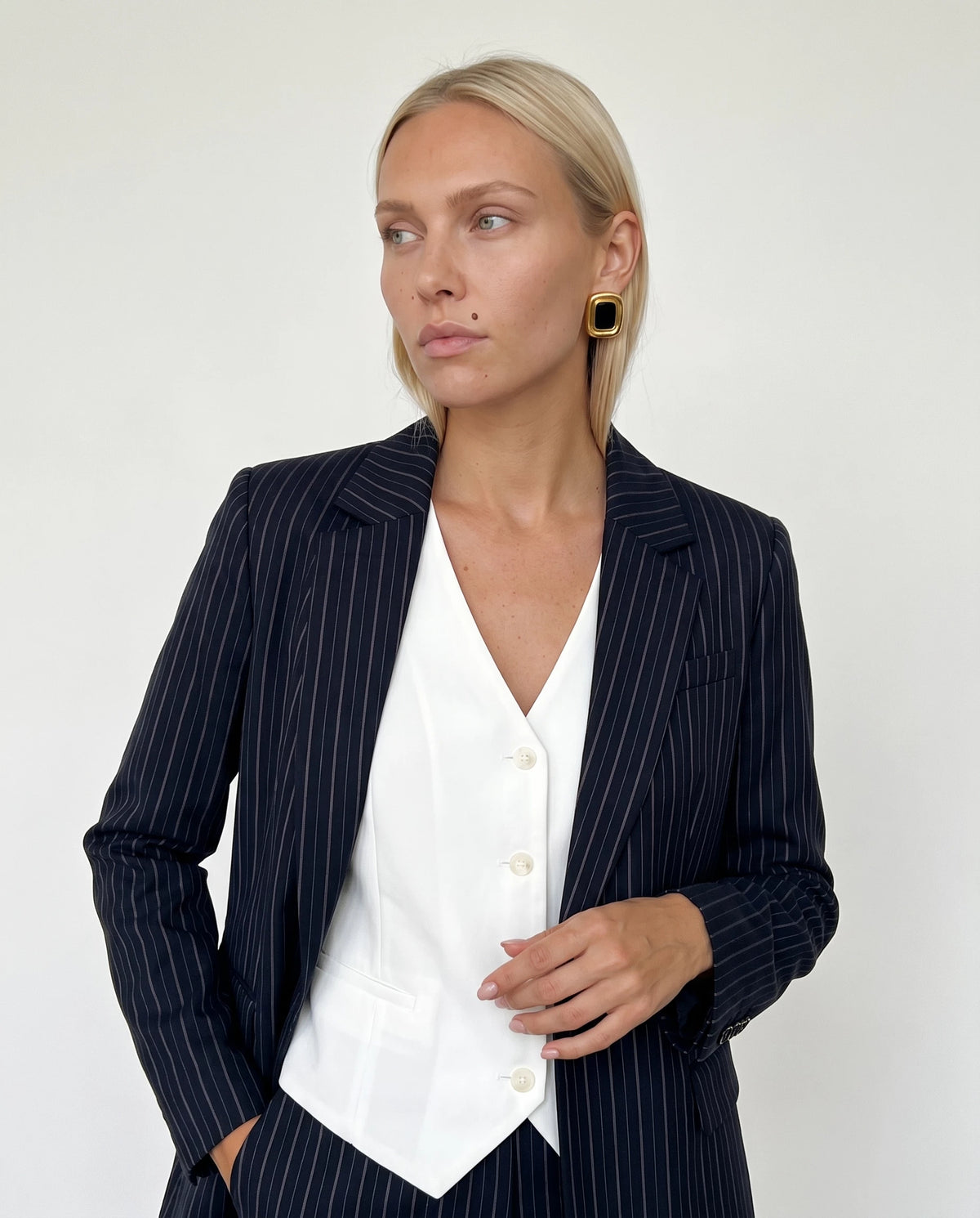 Woman in a navy pinstripe blazer and white vest wearing Sabine black and gold square statement stud earrings