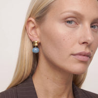 Close-up of a woman with blonde hair wearing an Ondine earring, a blue resin drop under a stacked gold stud, in a pinstripe blazer