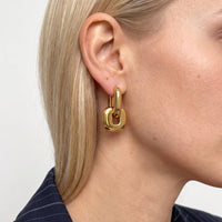 Close-up of a woman with blonde hair tucked behind her ear wearing a gold Edie square link hoop earring