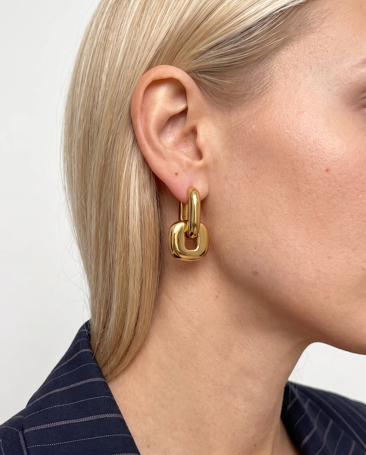 Close-up of a woman with blonde hair tucked behind her ear wearing a gold Edie square link hoop earring