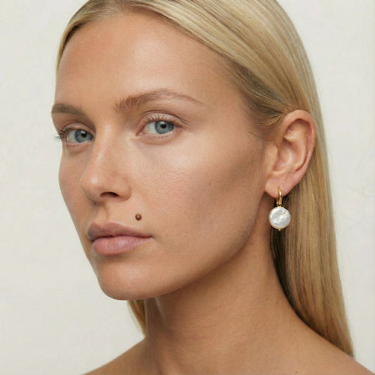 Close-up of a woman wearing pearl earrings against a plain background