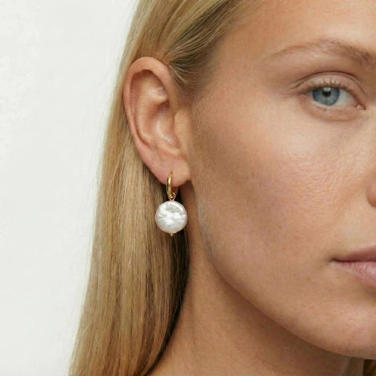 Close-up of a woman wearing pearl earrings with a plain background