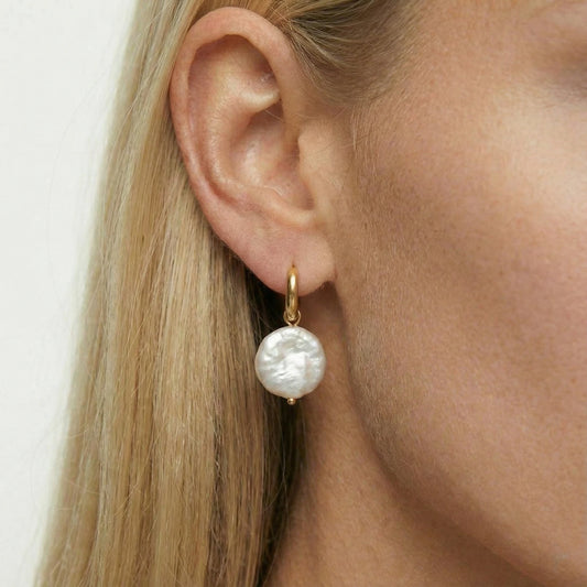 Pearl earring worn by a person with blonde hair on a white background