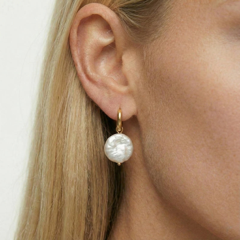 Pearl earring worn by a person with blonde hair on a white background