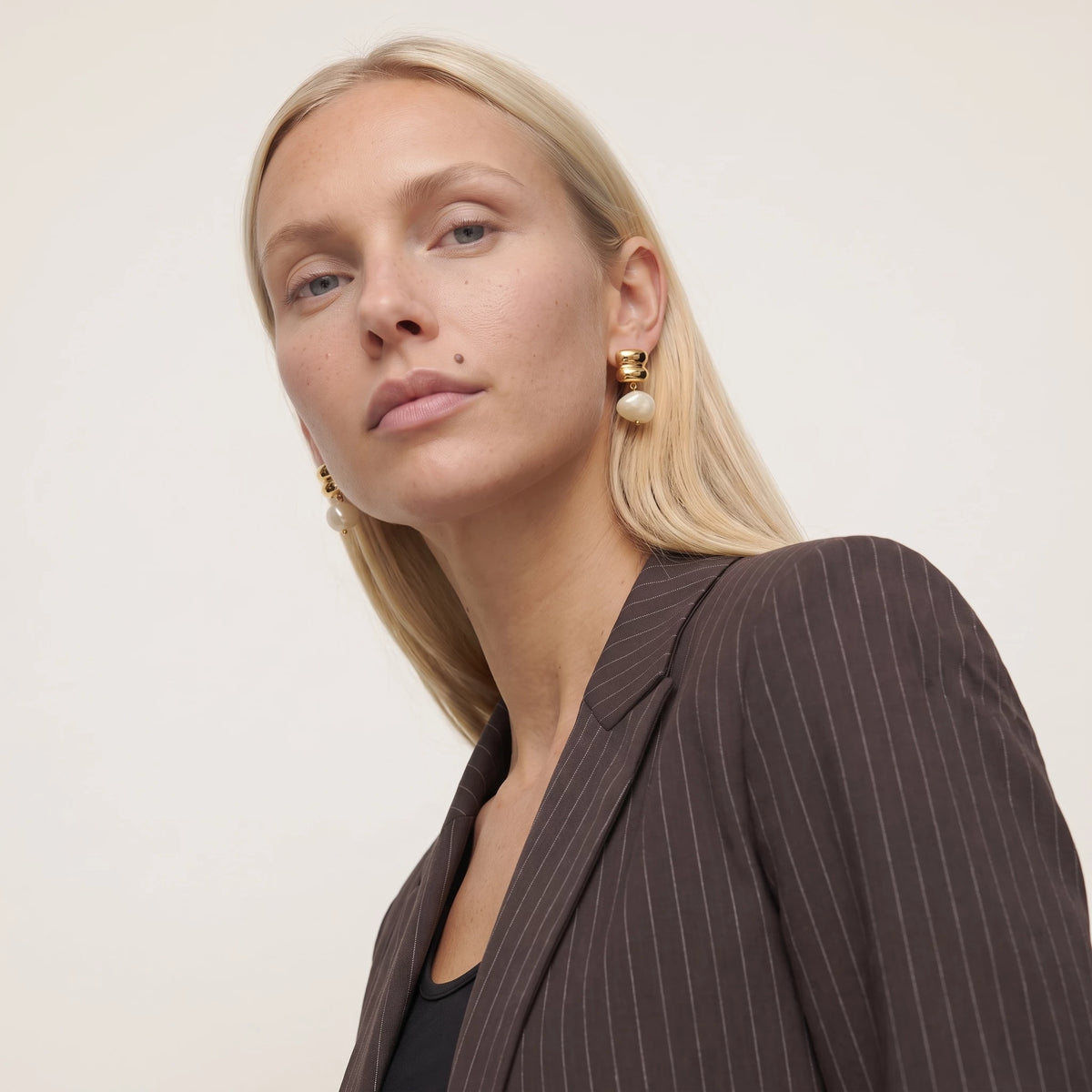 Woman with blonde hair in a brown pinstripe blazer and black top wearing the Bianca ivory resin drop earring