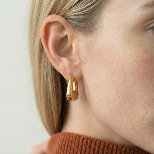 Close-up of a person wearing gold hoop earrings with a plain background