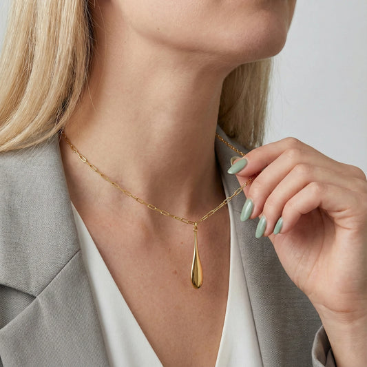 Modern gold teardrop pendant necklace in 18K gold plated stainless steel, worn on model with grey blazer