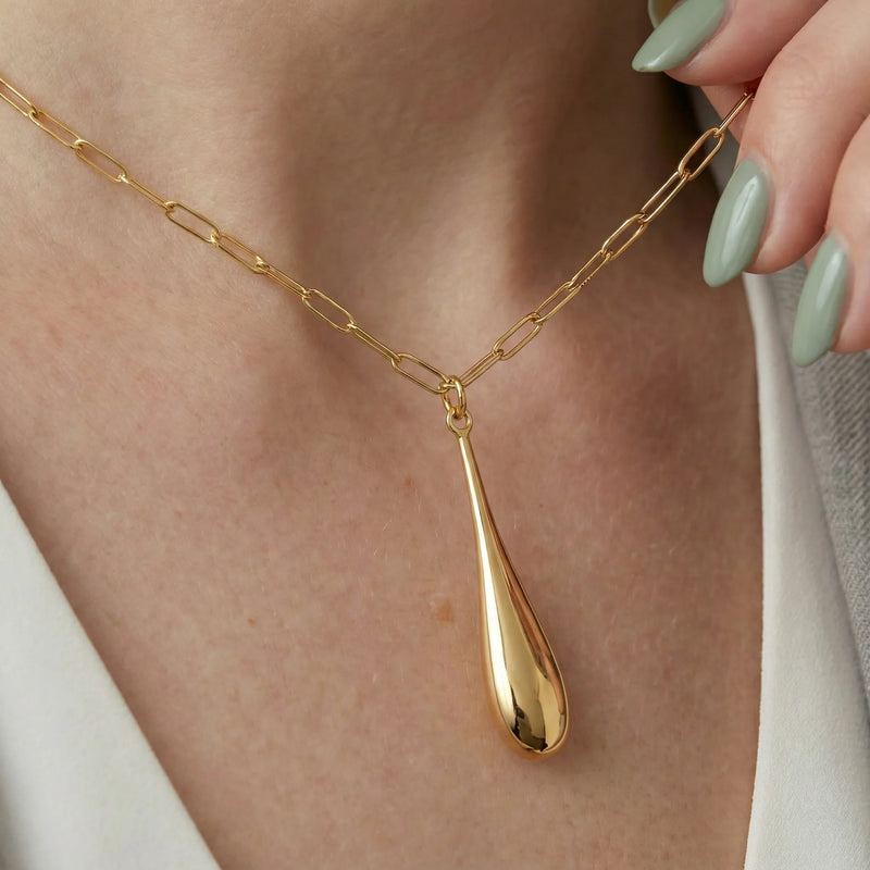 Gold necklace with a teardrop pendant worn by a person with light green nail polish.