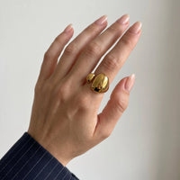 Hand with natural nails wearing the gold Romy dome ring on the middle finger, a navy pinstripe sleeve at the wrist