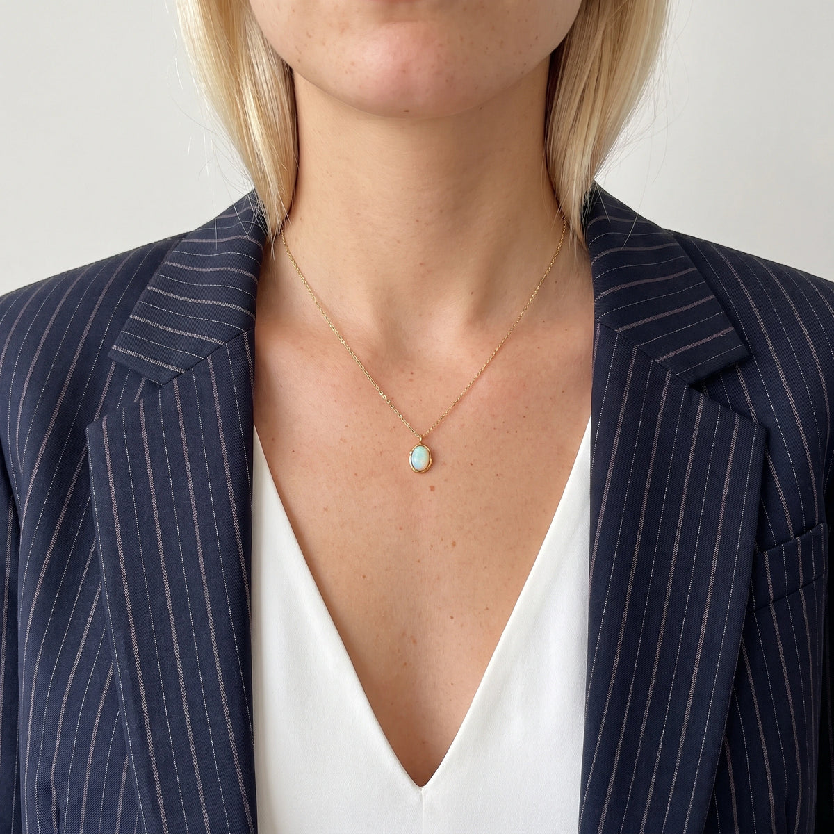 Ivy molten opal pendant necklace in 18K gold-plated waterproof stainless steel, worn with a navy pinstripe blazer and white top