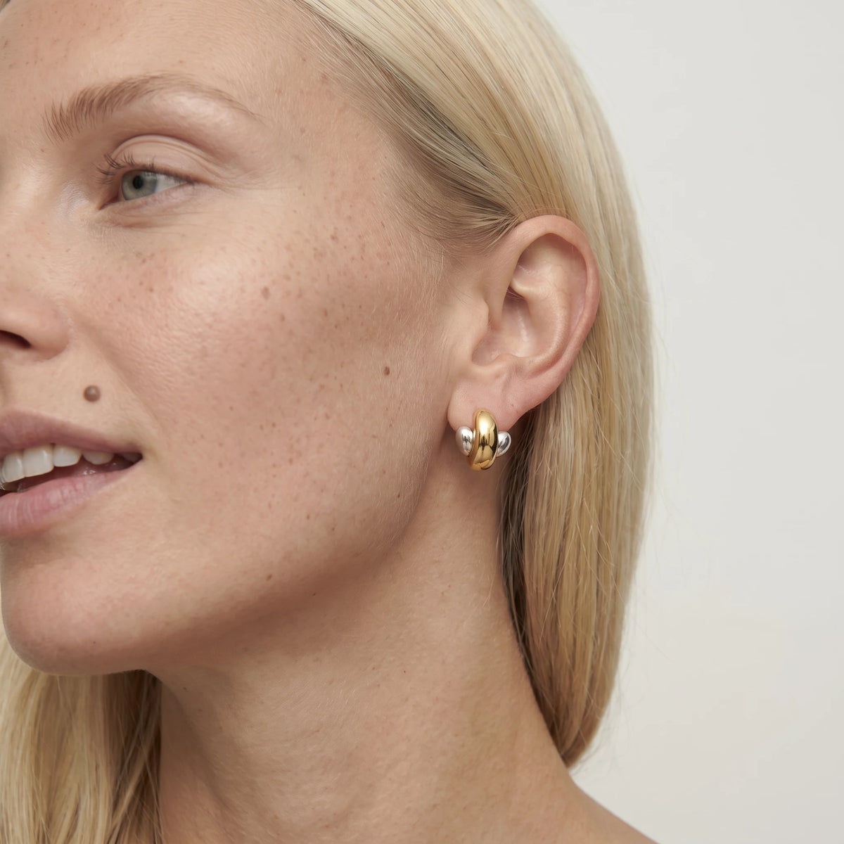 Close-up of a woman with blonde hair in side profile wearing an Esme duo tone crossed stud, a gold loop over silver ends
