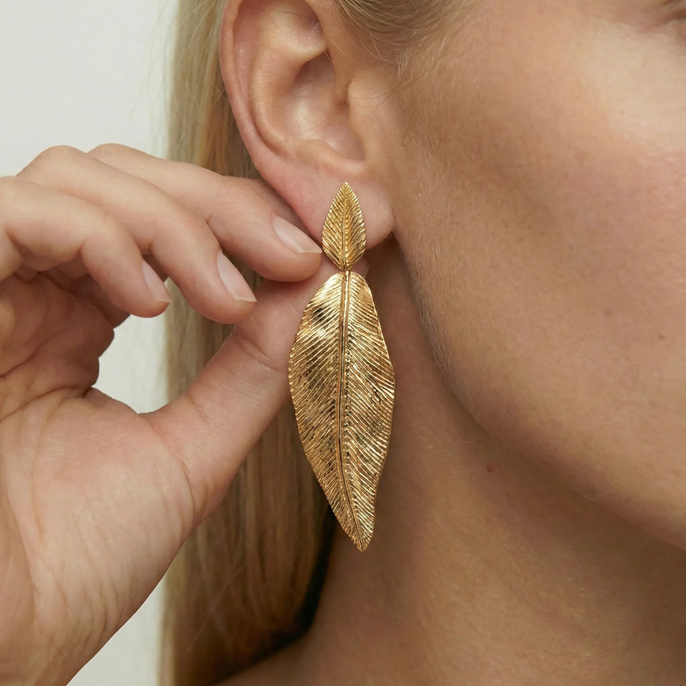 Gold leaf earring being worn on a person's ear with a neutral background