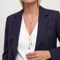 Woman in a navy pinstripe blazer and white vest wearing the gold Elodie lariat, its teardrop drops falling to mid-chest