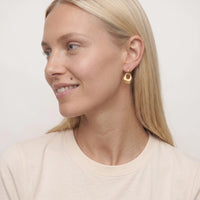 Woman with blonde hair smiling in side profile wearing a gold Agnes molten drop huggie, in a cream t-shirt